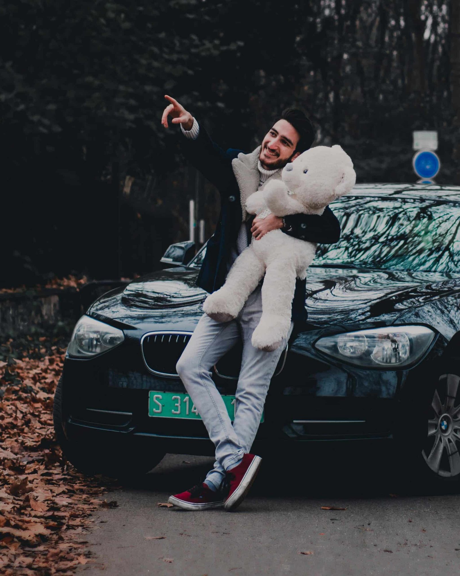 Adulte tenant une peluche d’ours devant une voiture, symbole de tendresse assumée à l’âge adulte